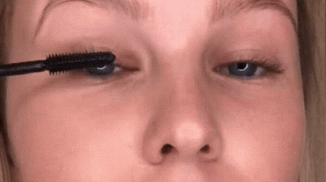 a woman is applying mascara to her eyelashes with a brush .