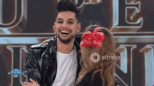 a man in a leather jacket is laughing with a woman in a red bow in her hair ..