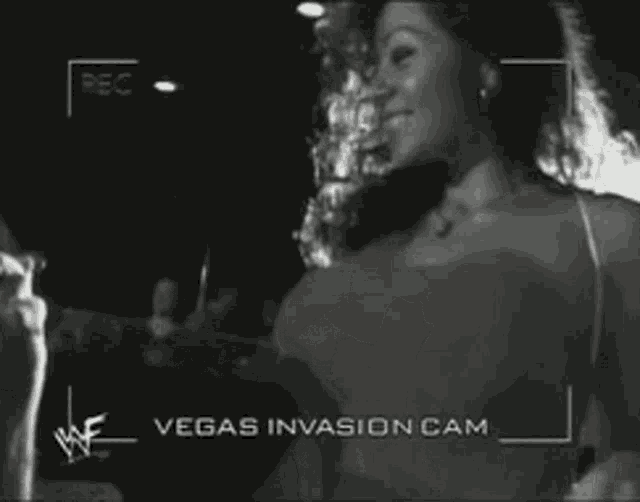 a woman is singing into a microphone while being filmed by a vegas invasion cam .