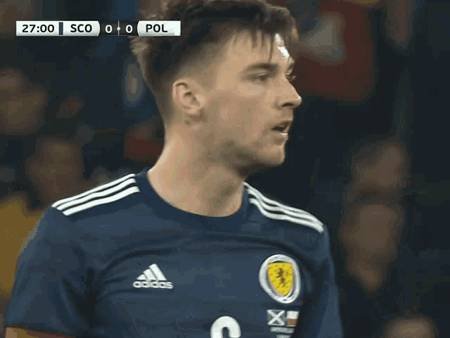 a soccer player wearing an adidas jersey looks at the scoreboard