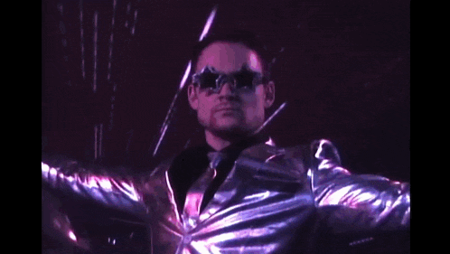 a man in a silver jacket and sunglasses is standing in a dark room