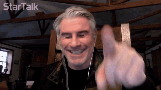 a man wearing ear buds is smiling and pointing at the camera with the words startalk above him