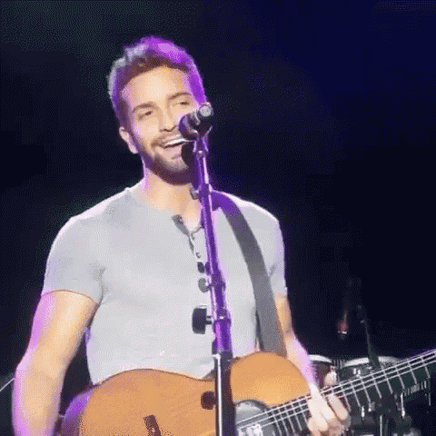a man is singing into a microphone while holding a guitar on stage .