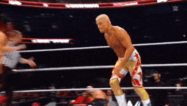 a wrestler is standing in a wrestling ring with a referee in the background .