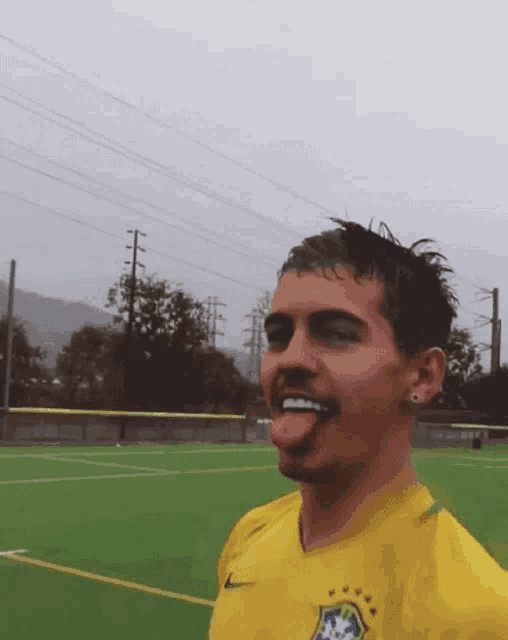 a man wearing a yellow shirt with the brazilian flag on it sticks out his tongue