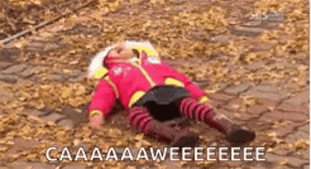 a little girl is laying on the ground covered in leaves and screaming .