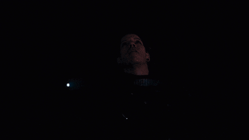 a man in a dark room with a light behind him that says ' moschino ' on it