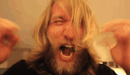 a man with long blonde hair and a beard screams with his mouth open