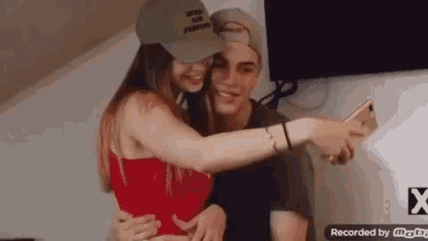 a man and a woman are hugging and taking a selfie with their cell phone .