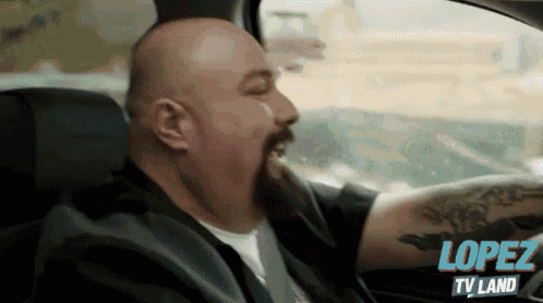 a bald man with a beard is driving a car with lopez tv land written on the bottom