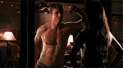a man without a shirt is flexing his muscles in front of a woman in a dark room .