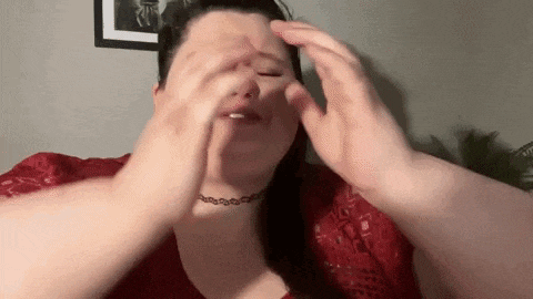 a woman is covering her face with her hands while wearing a choker necklace .