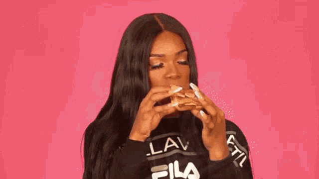 a woman in a fila shirt is eating a hamburger .