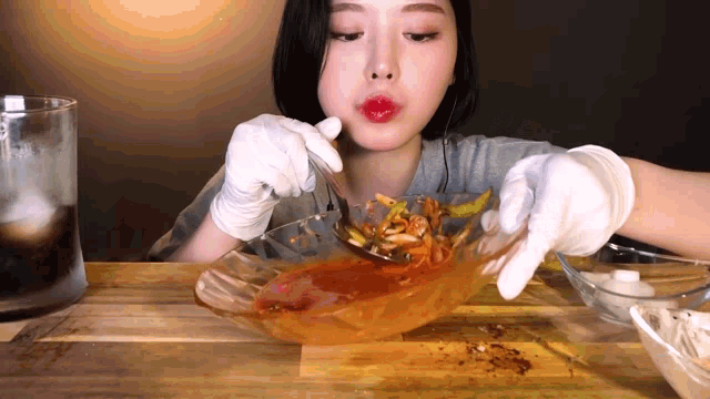 a woman wearing gloves is eating a bowl of food with a spoon