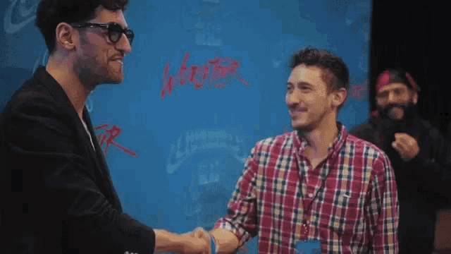two men shaking hands in front of a wall that has the word winter written in red