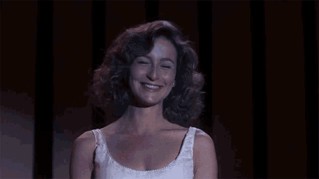 a woman in a white tank top is smiling and looking at the camera