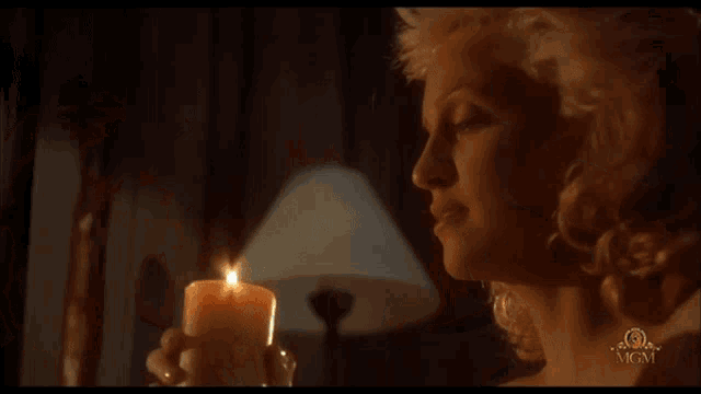 a woman is holding a lit candle in front of a lamp with mgm written on the bottom
