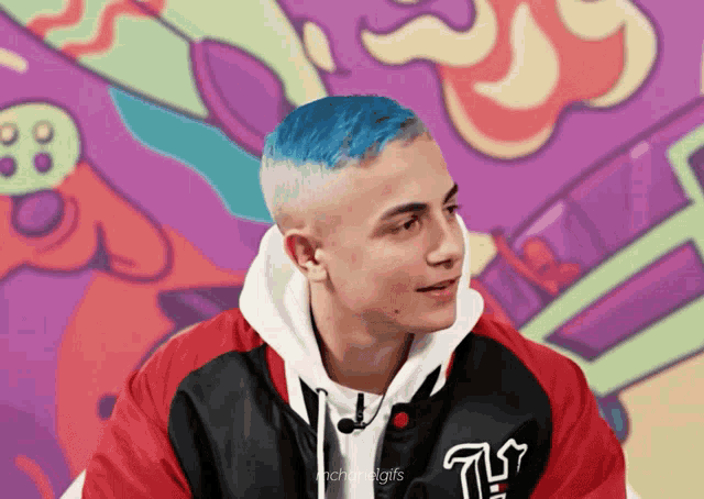 a man with blue hair is wearing a black and red jacket with the letter t on it
