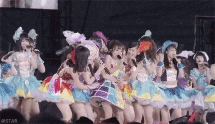 a group of girls in colorful dresses are singing into microphones on a stage