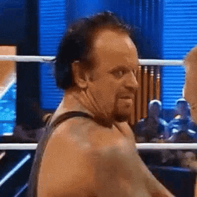 a man with a beard is standing in a wrestling ring and looking at the camera .