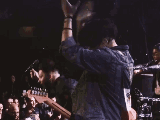 a man in a denim jacket is singing into a microphone while playing a guitar