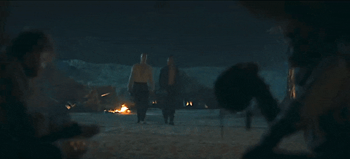 a group of people are standing around a fire at night .