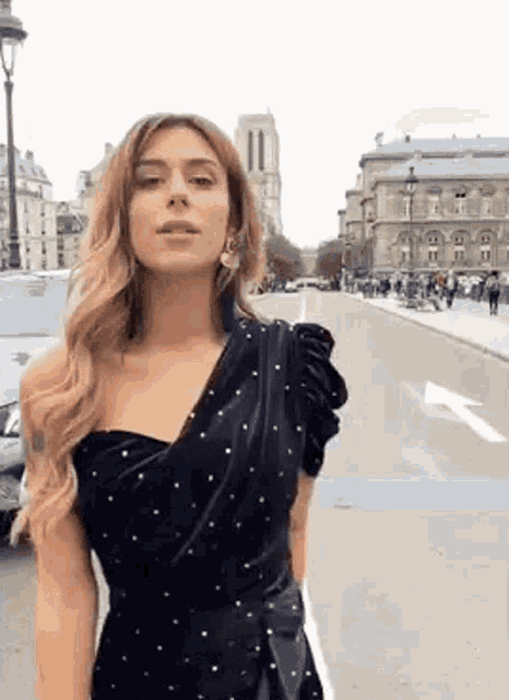 a woman in a black dress is standing on the side of a street .