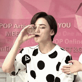 a woman in a polka dot shirt is drinking from a clear glass