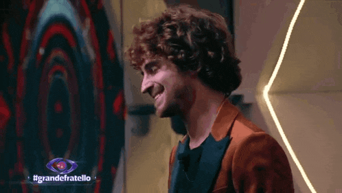 a man with curly hair is smiling in front of a sign that says grande fratello