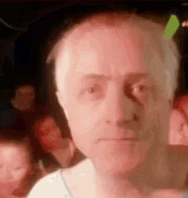 a close up of a man 's face with a blurry background of people behind him .
