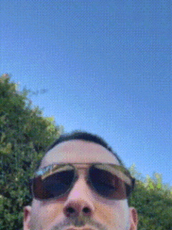 a man wearing sunglasses is taking a picture of himself against a blue sky .