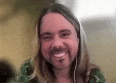a man with long hair and a beard is smiling for the camera while wearing headphones .