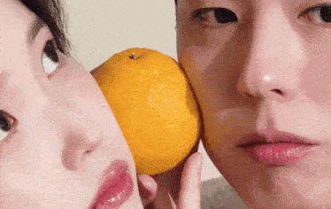 a man and a woman are touching their faces with an orange between them