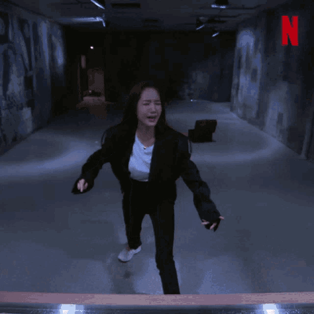 a woman in a black suit is running in a dark hallway with the word nooo on the bottom