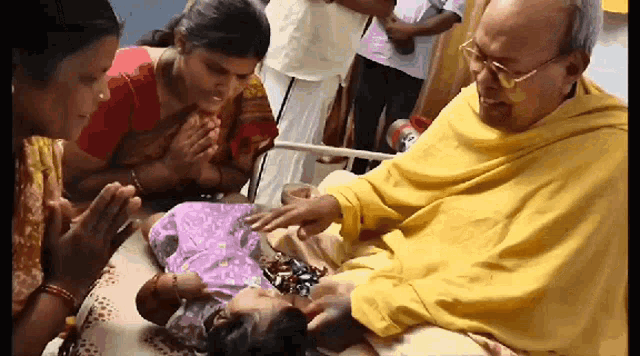 a man in a yellow robe is touching a baby 's face