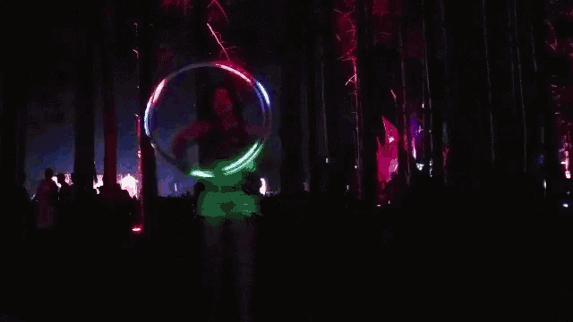 a woman is holding a glowing hula hoop in a dark forest