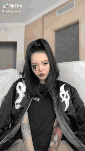 a woman with a tattoo on her face is wearing a black jacket with a dragon on it .