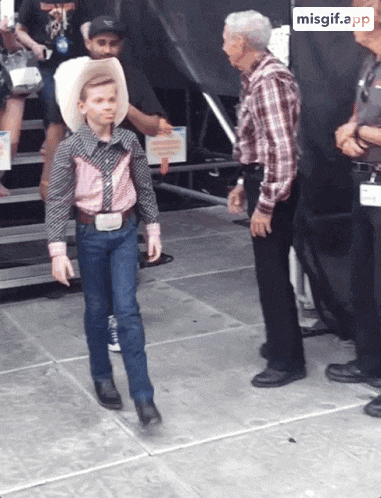 a young boy in a cowboy outfit is walking across a stage with a missgif.app watermark on the bottom