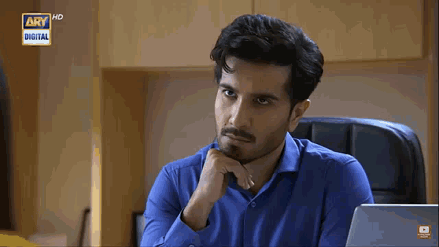 a man in a blue shirt is sitting in front of a laptop with ary digital written on the bottom