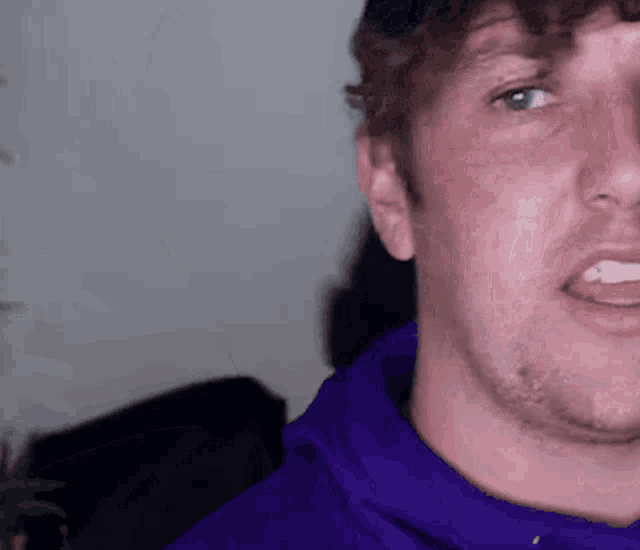 a close up of a man 's face wearing a purple shirt and a hat .