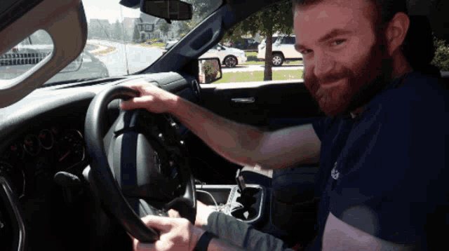 a man with a beard is sitting in a car holding the steering wheel