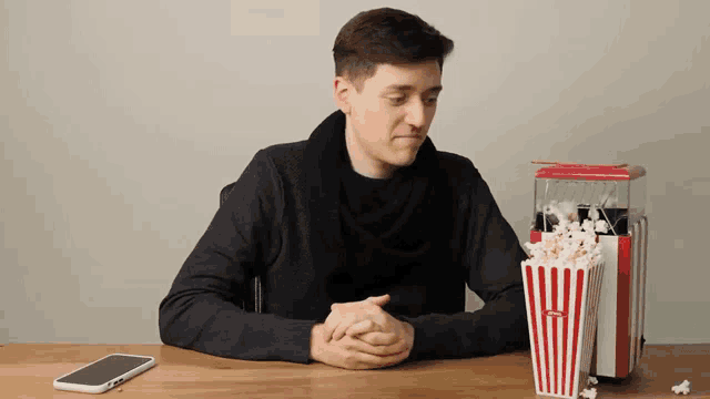 a man sits at a table with a popcorn maker and a phone