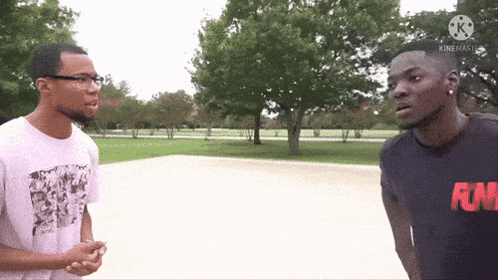 two men are standing next to each other in a park and one has a raw shirt on .