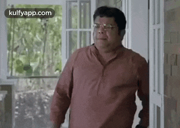 a man in a red shirt and glasses is standing in front of a white door .