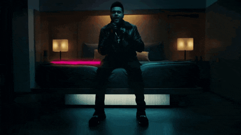 a man in a leather jacket sits on a bed