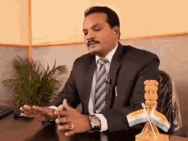 a man in a suit and tie is sitting at a desk in front of a statue of the indian flag .