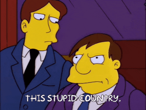 two men in suits and ties are standing next to each other and one of them says " this stupid country "