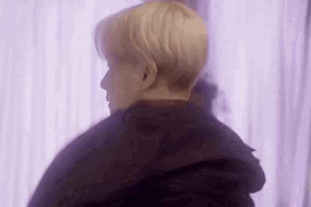 a man with blonde hair is standing in front of a purple curtain and looking at the camera .