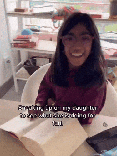a girl with glasses sits at a desk with a book and says sneaking up on my daughter
