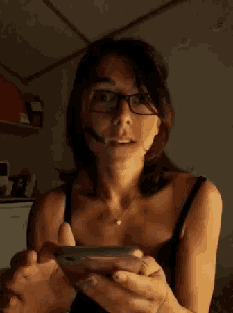 a woman wearing glasses is smiling while holding a cell phone in her hand .